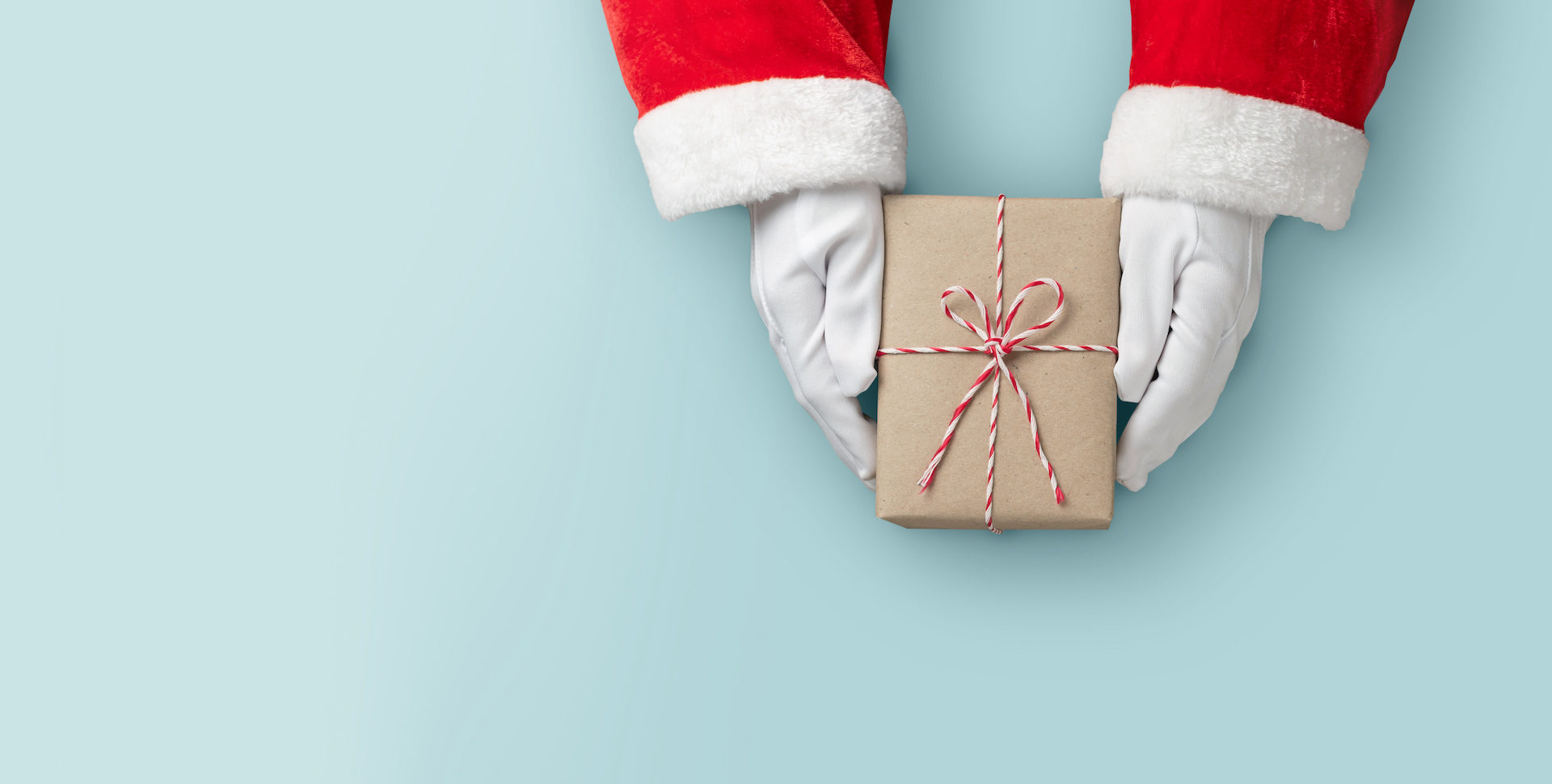 Top view of Santa claus hands is holding a brown gift box or present box over blue isolated background.
